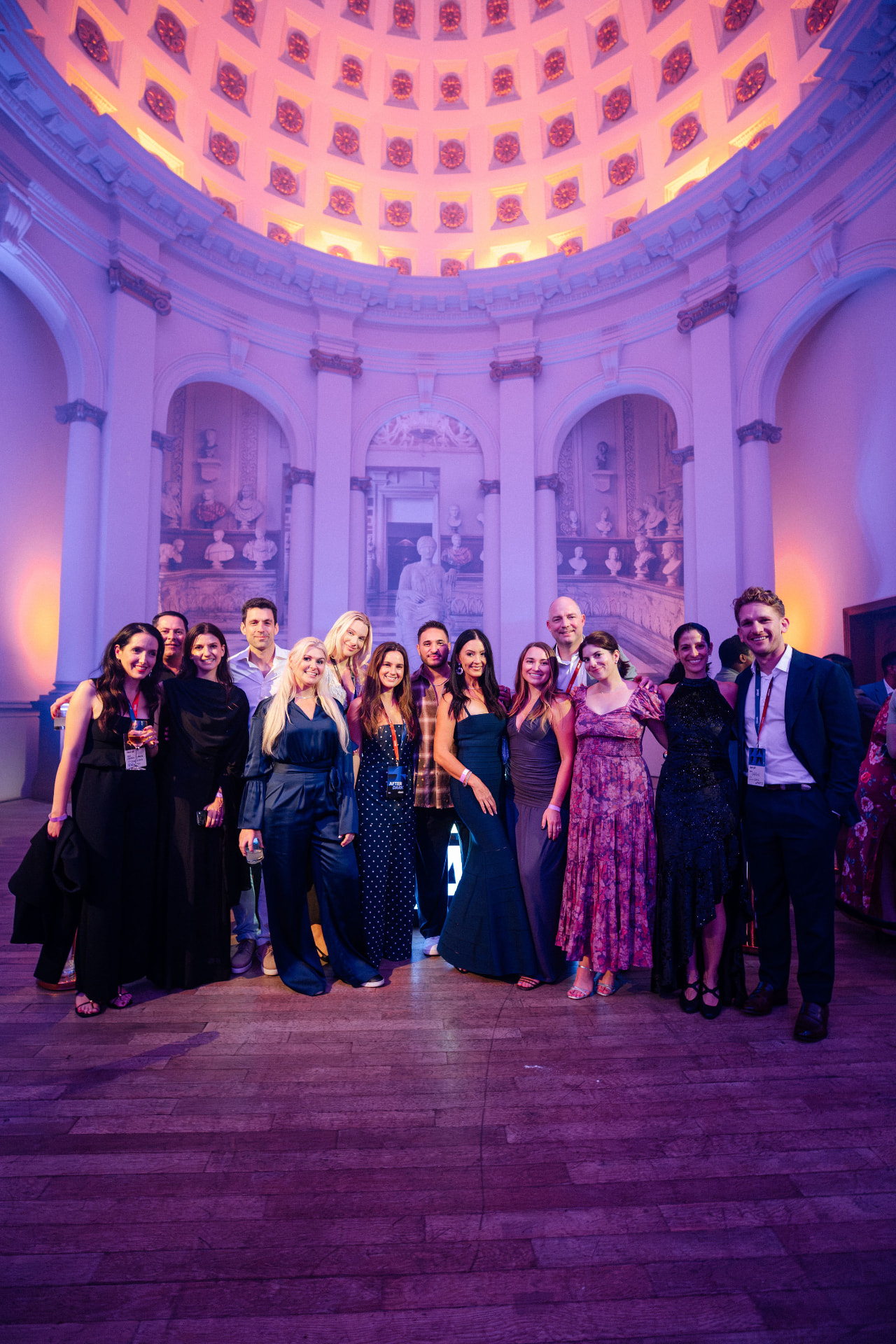 A group of guests posing together on the floor of the former church beneath the coffered dome, lit in violet and amber