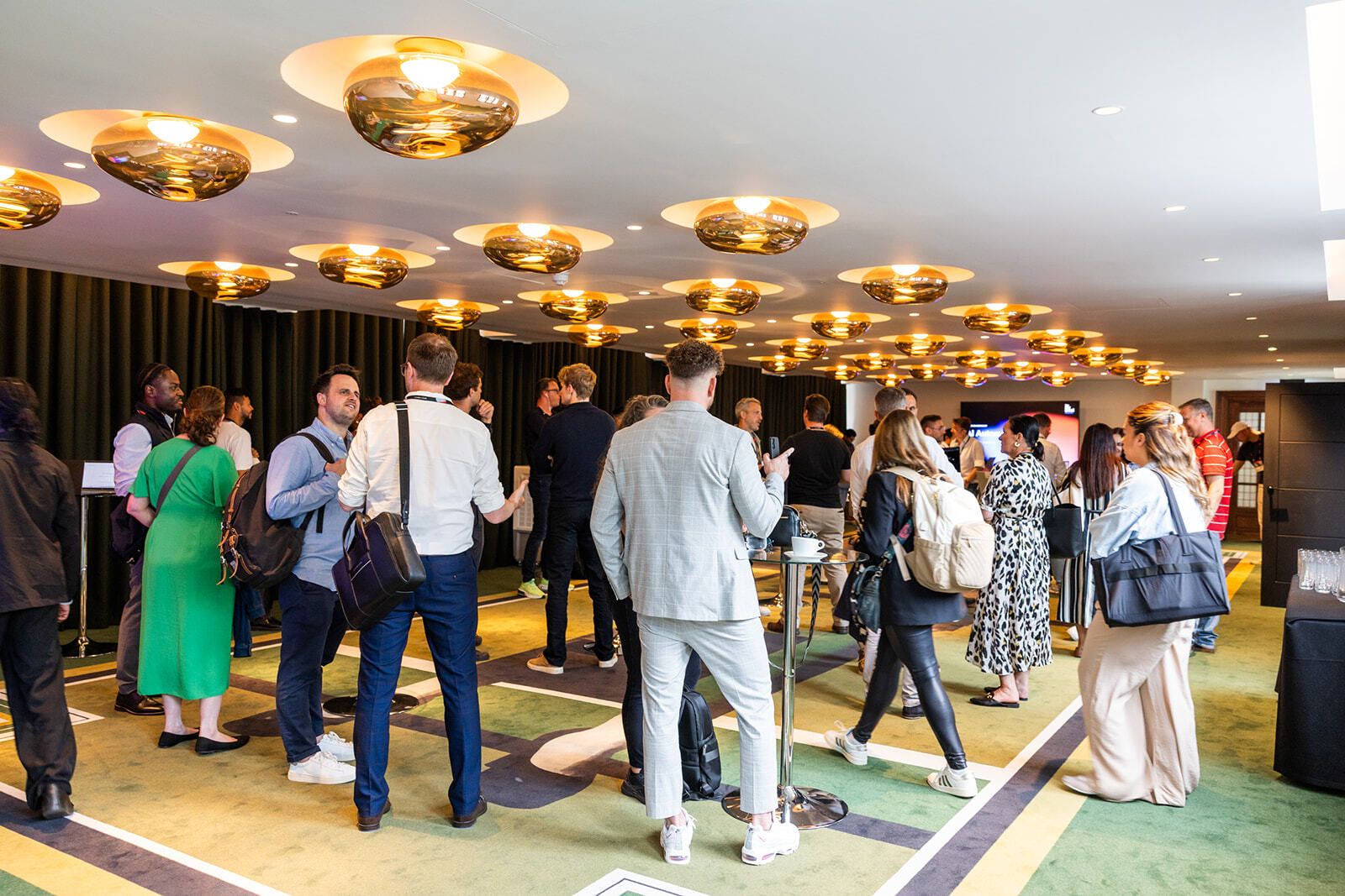 Guests networking between sessions beneath gold pendant lighting