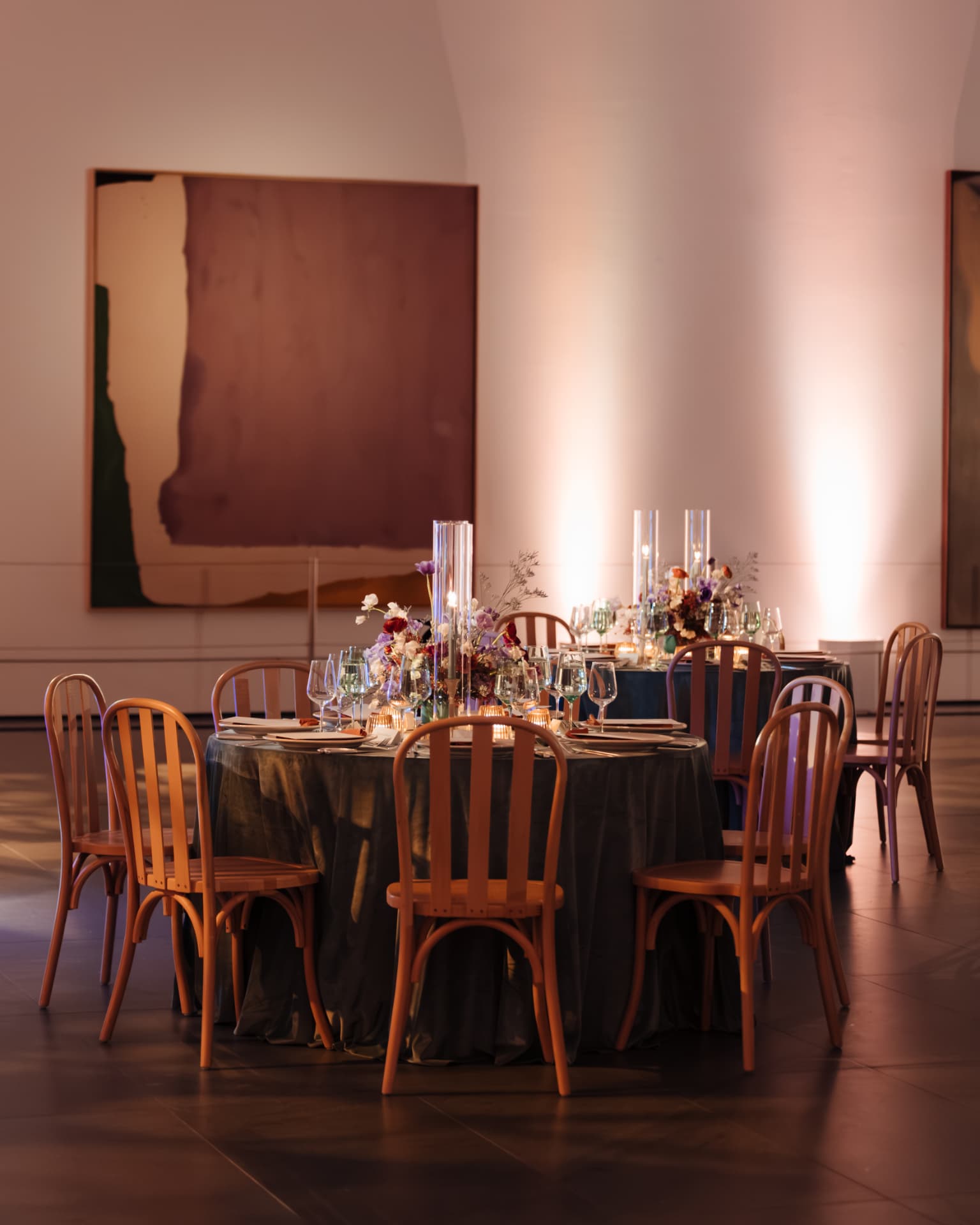 Candlelit round tables set with florals in front of a large painting