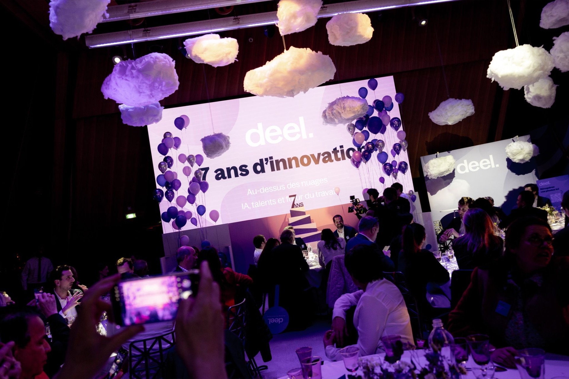 Guests seated beneath cloud installations as the screen reads 7 ans d'innovation