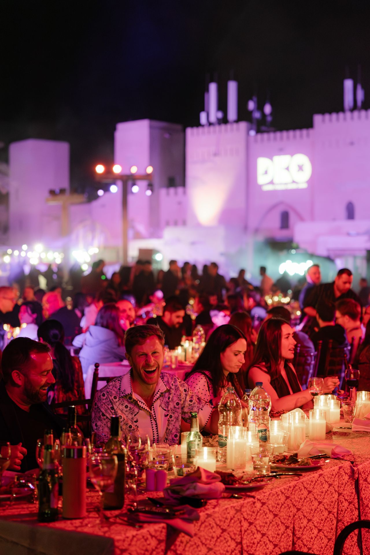 Candlelit long tables at the Global Kickoff desert dinner, with an illuminated fort behind the crowd