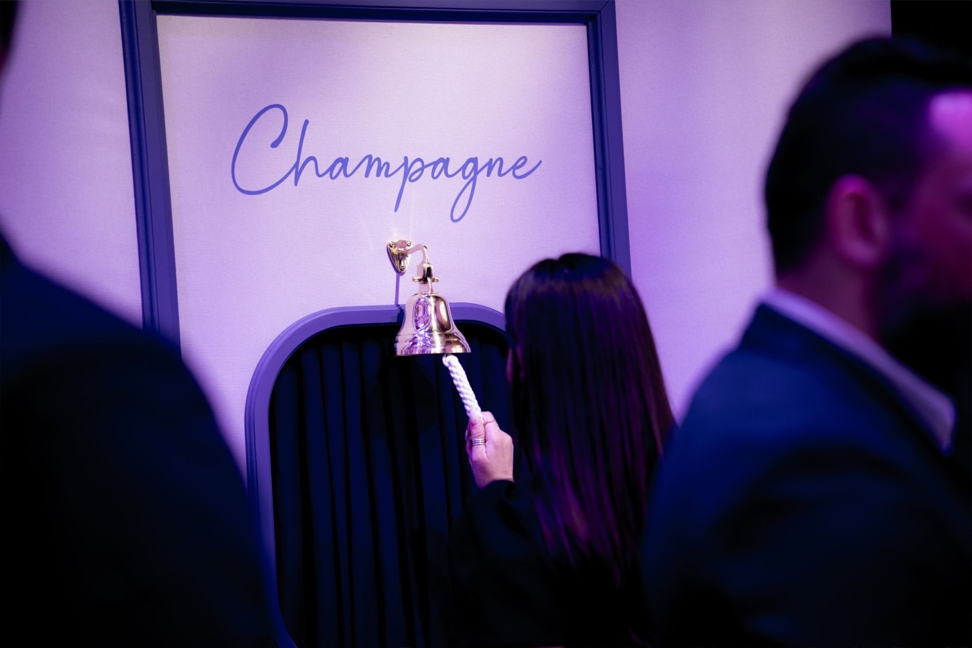 A guest ringing the brass champagne bell beneath a Champagne sign