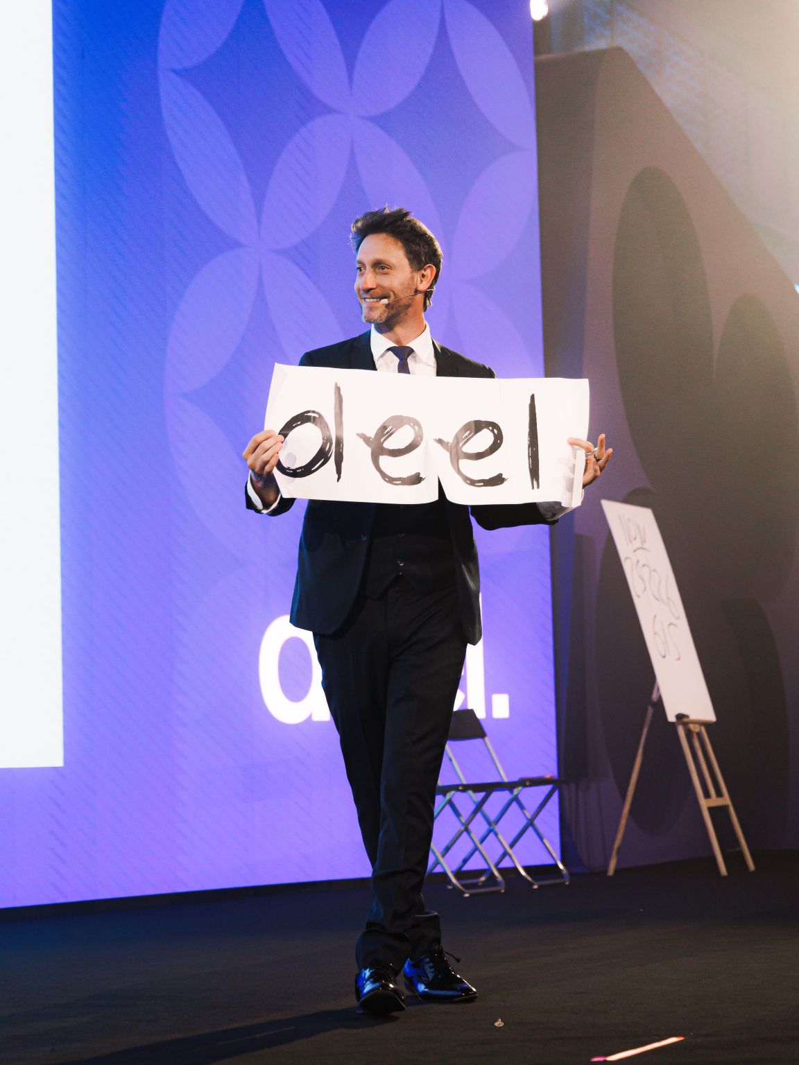 Lior Suchard on the main stage holding hand-drawn deel letter cards during an interactive mentalism session