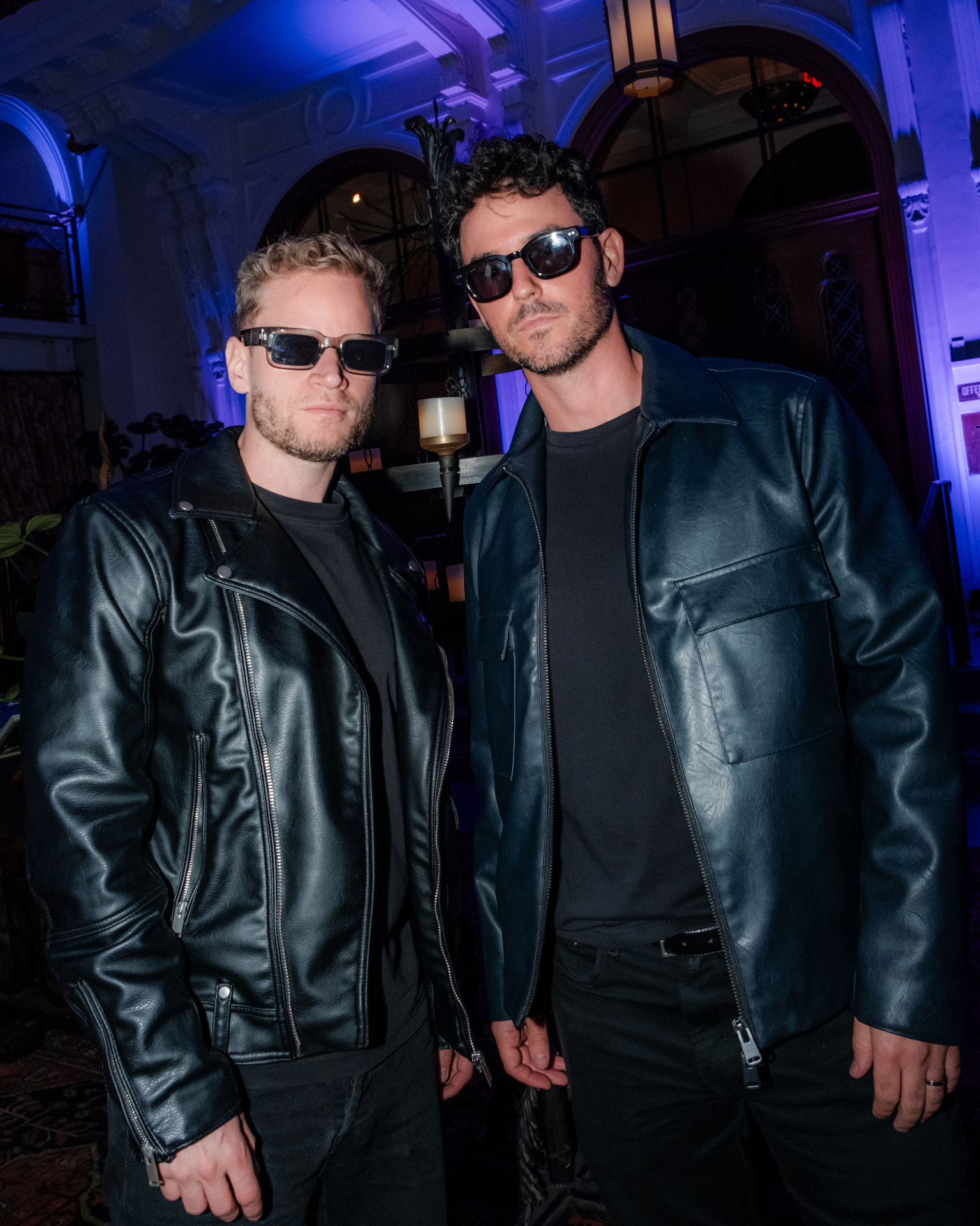 Two guests in sunglasses posing beneath blue-lit stone arches inside the former church