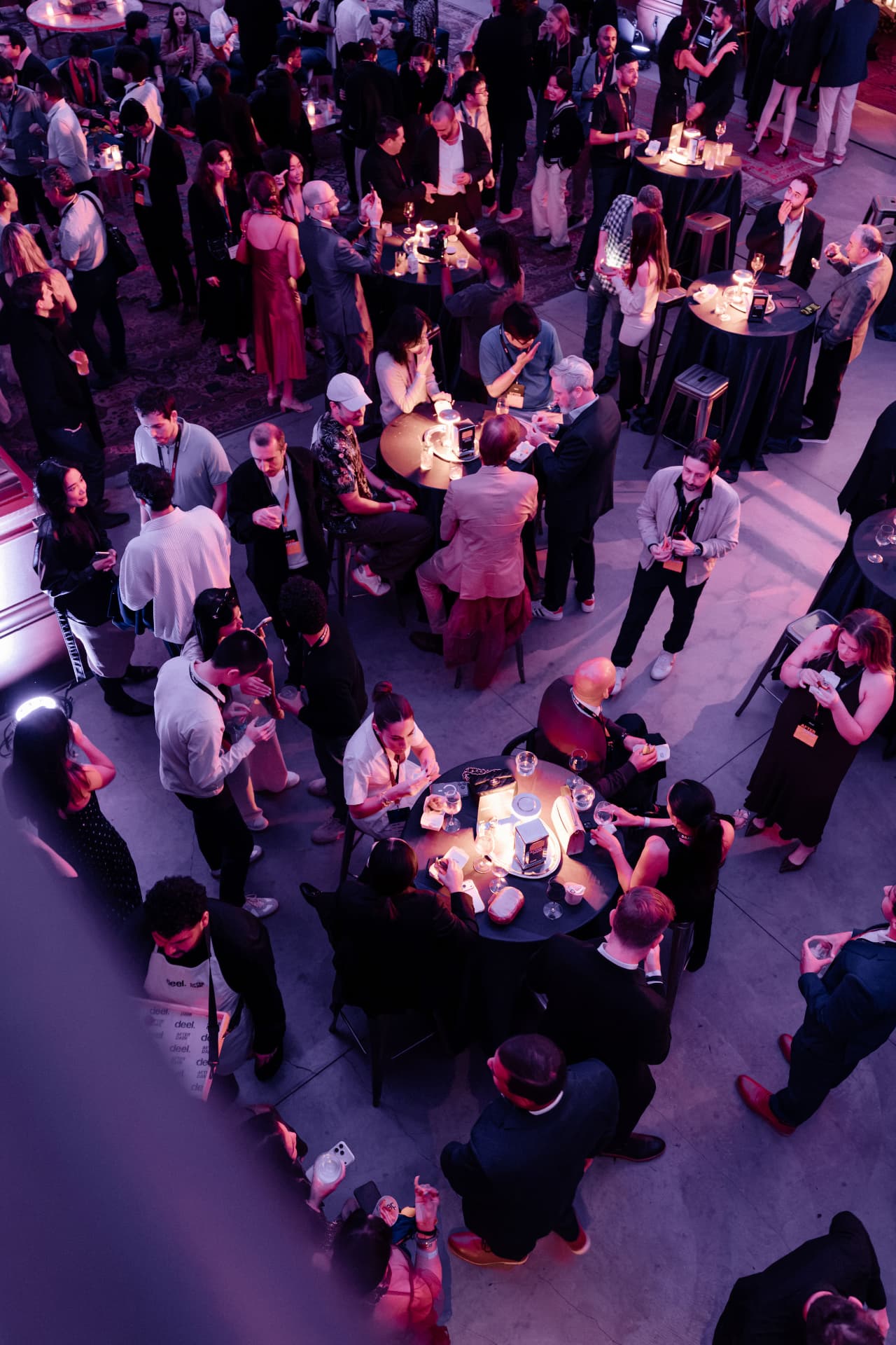 Guests gathered around illuminated cocktail tables on the event floor beneath violet lighting